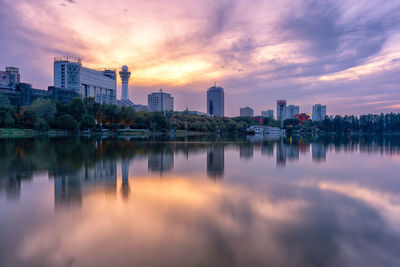 Scenic view of lake by buildings against sky during sunset