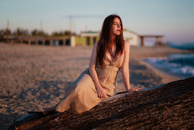 Young woman sitting on land against sky during sunset