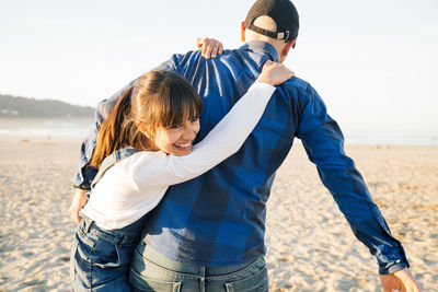 Father carrying daughter while walking at beach