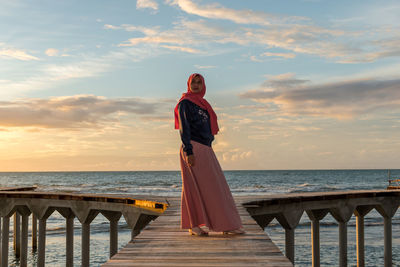 Woman standing at beach against sky during sunset