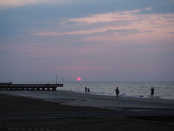 People on beach against sky during sunset