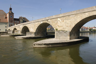 Arch bridge over river by buildings against sky