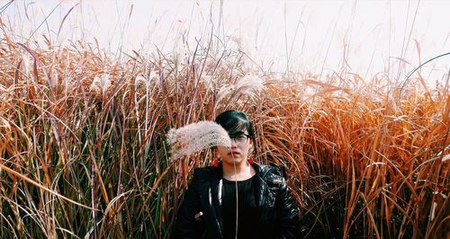 Portrait of young woman standing by grass on field