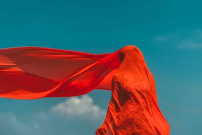 Woman covered with red fabric while standing against sky