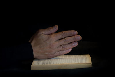 Close-up of hand holding book against black background