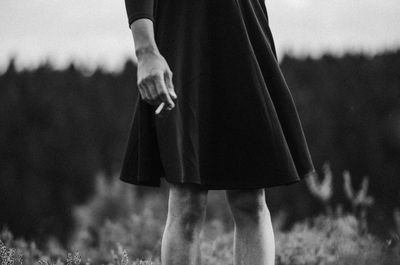 Midsection of woman holding cigarette while standing by plants