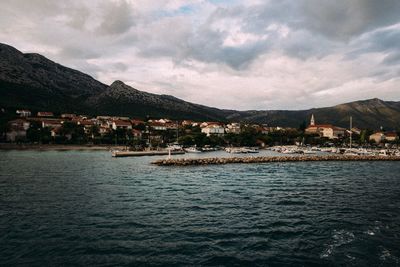 Sea by buildings in town against sky