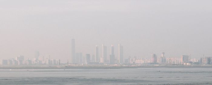 Sea by modern buildings in city against sky