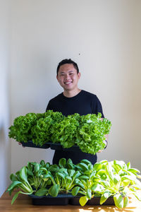 Portrait of smiling man holding vegetables while standing against wall at home