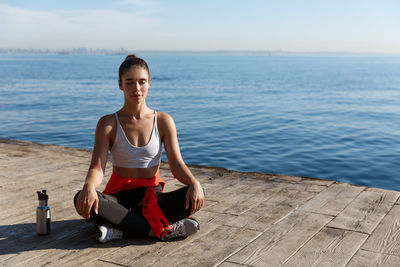 Young woman meditating on road against sea