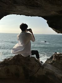 Rear view of woman sitting on rock at beach