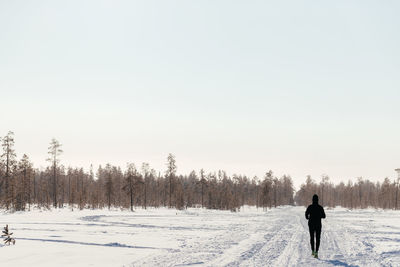 Sporty man in sportswear running through a winter park, rear view. copying space