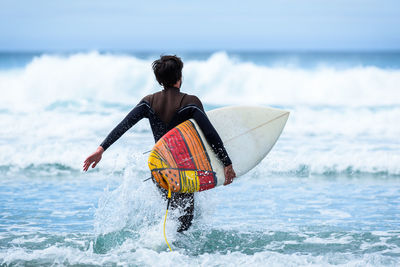 Rear view of man with surfboard walking in sea