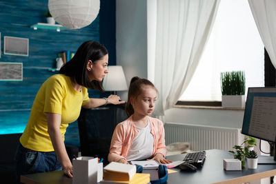 Mother assisting daughter while using computer at home office