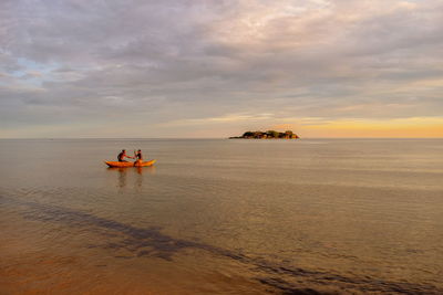 Men on boat sailing in sea against sky during sunset