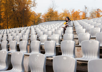 Woman holding leaf sitting on chair in stadium park