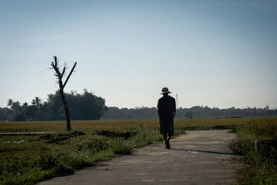 Rear view of man walking on road against clear sky