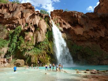 People on rock against waterfall and sky