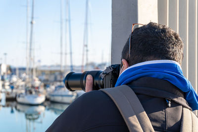 Rear view of a man taking photos in an indiscreet way with a professional camera with a zoom lens.