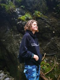 Smiling young woman standing by tree in forest