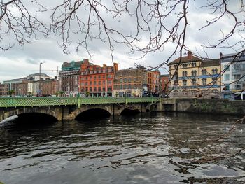 Bridge over river by buildings against sky in city