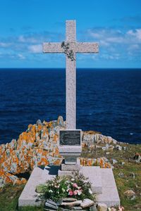 Cross on beach by sea against sky