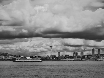 Sea and space needle amidst towers against cloudy sky