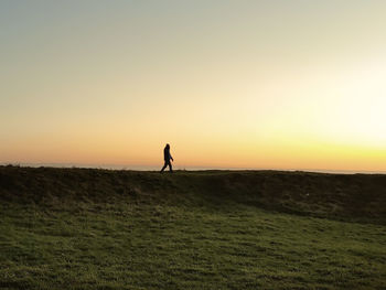 Silhouette person on field against sky during sunset