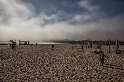 People on beach against cloudy sky