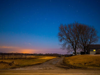 Road by bare trees on field against sky at night