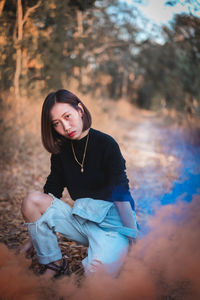 Full length of woman holding distress flare while crouching in forest