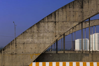 Low angle view of bridge against buildings against blue sky