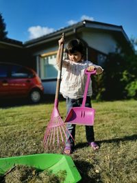 Full length of girl holding gardening equipment at yard on sunny day