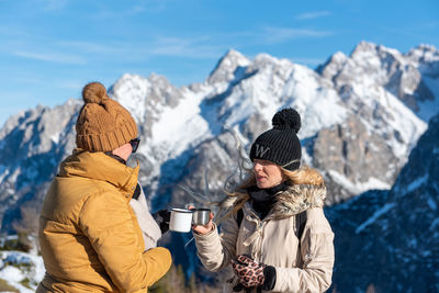 Two female friends drinking tea in mountains on a sunny day in winter