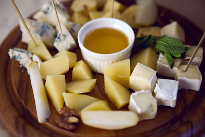 Different sliced cheese is on a wooden plate with honey