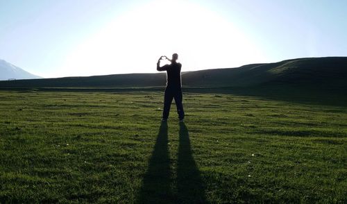 Silhouette man making heart shape while standing on field against sky
