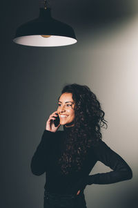 Young woman using phone while standing against wall