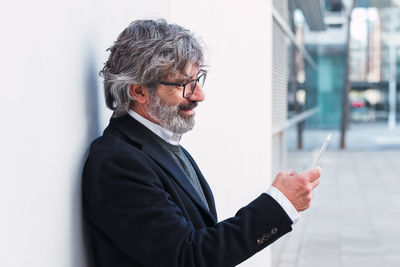 Senior businessman using mobile phone, typing message to partners after conference