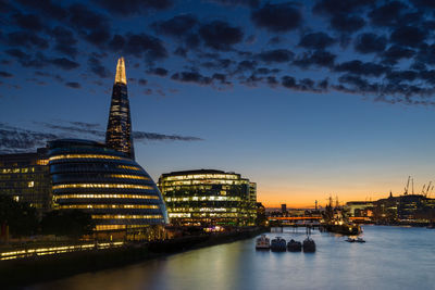 Illuminated modern buildings in city by thames river against sky