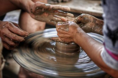 Cropped hands of potters making earthenware on pottery wheel