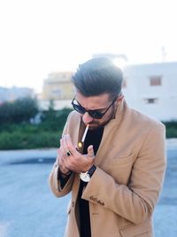 Young man wearing sunglasses igniting cigarette while standing outdoors