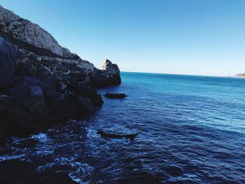 Rock formations in sea against clear blue sky