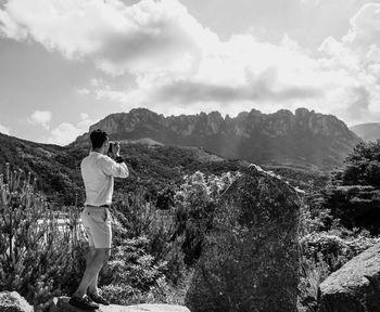Side view of man photographing mountain against sky