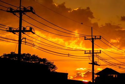 Low angle view of silhouette electricity pylons against orange sky