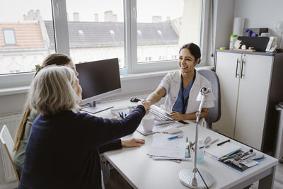 Senior woman doing handshake with female doctor at desk in clinic