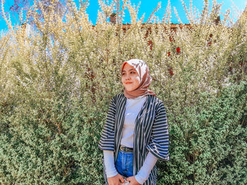 Young woman looking away while standing by plats outdoors