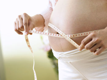Midsection of pregnant woman measuring belly with tape measure