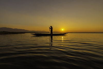 Silhouette man in sea against sky during sunset