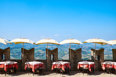 Tables and chairs with parasols arranged against blue sky during sunny day