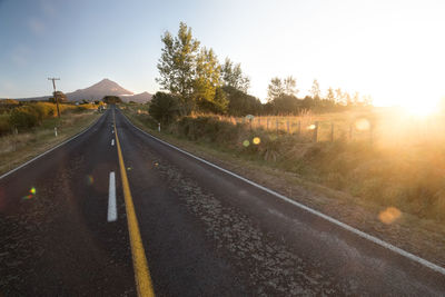 Road by trees against sky during sunset